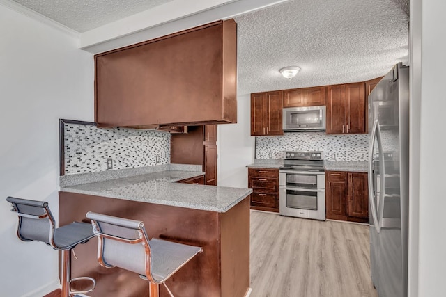 kitchen featuring a kitchen breakfast bar, appliances with stainless steel finishes, kitchen peninsula, and tasteful backsplash