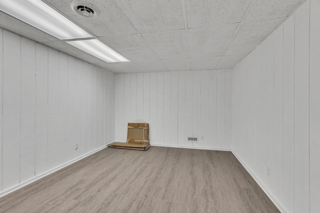 unfurnished room featuring a drop ceiling, light hardwood / wood-style flooring, and wooden walls