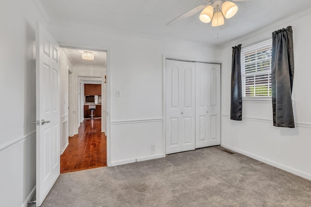 unfurnished bedroom with ceiling fan, a closet, light colored carpet, a textured ceiling, and ornamental molding