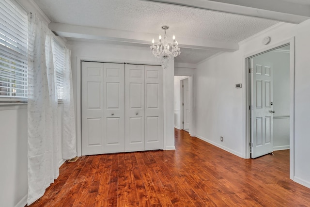 unfurnished bedroom with a textured ceiling, a closet, a chandelier, and beamed ceiling