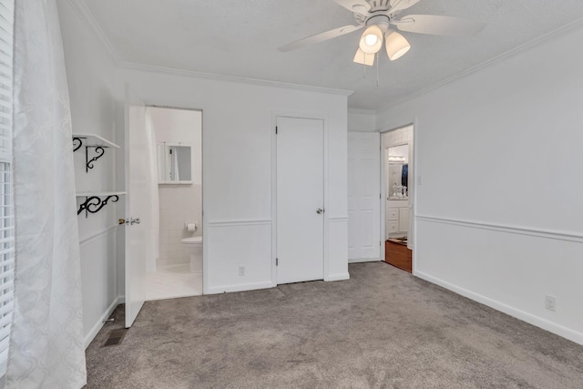 unfurnished bedroom featuring ensuite bath, ceiling fan, carpet floors, and crown molding