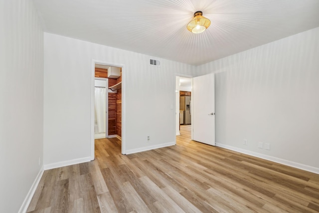 unfurnished bedroom featuring stainless steel fridge with ice dispenser, a closet, a walk in closet, and light hardwood / wood-style flooring