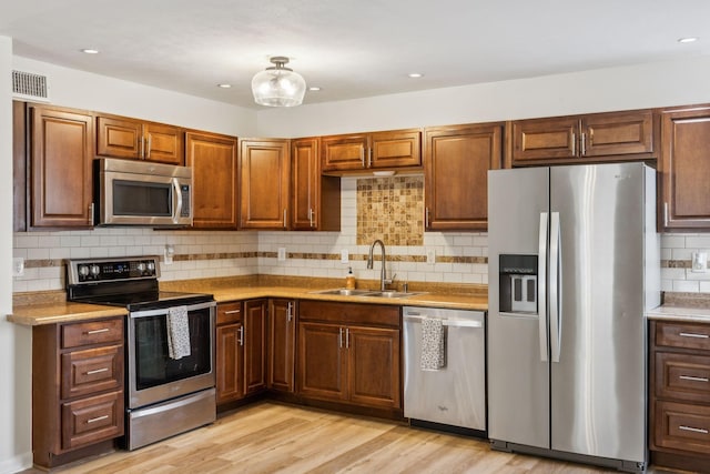 kitchen featuring sink, backsplash, light hardwood / wood-style floors, and appliances with stainless steel finishes