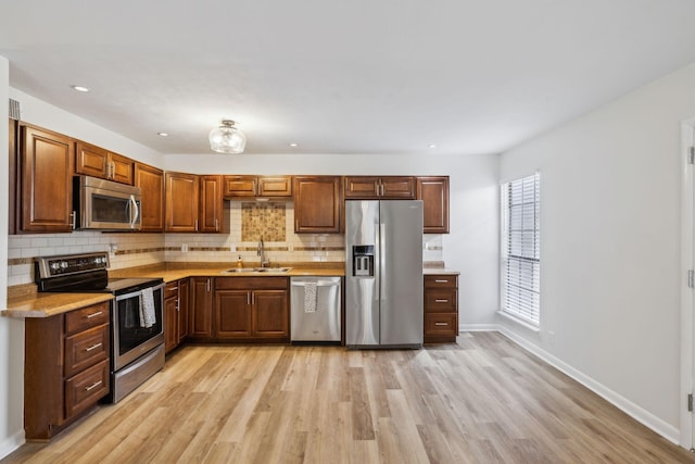 kitchen with sink, light hardwood / wood-style floors, appliances with stainless steel finishes, and decorative backsplash