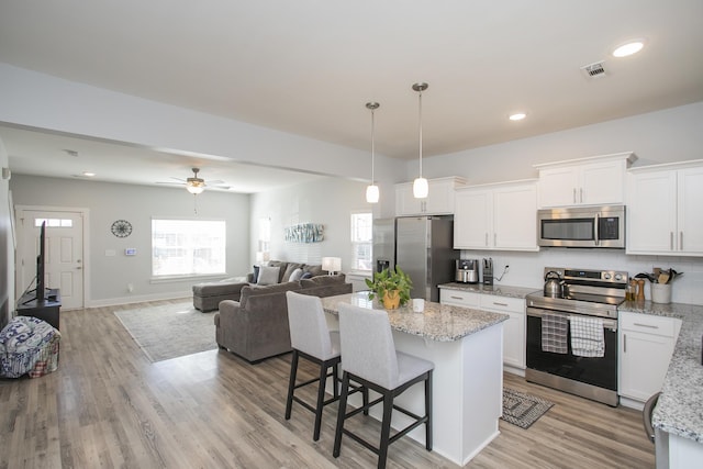 kitchen with hanging light fixtures, light wood-type flooring, appliances with stainless steel finishes, and white cabinetry