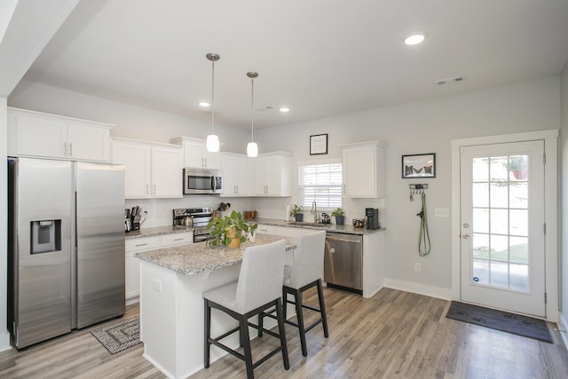 kitchen with white cabinetry, stainless steel appliances, decorative light fixtures, a kitchen island, and sink