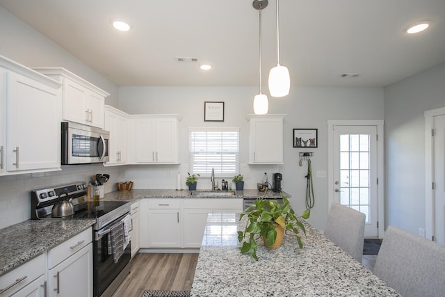 kitchen with sink, white cabinetry, hanging light fixtures, light stone countertops, and stainless steel appliances