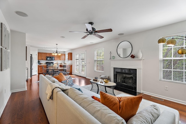 living room with ceiling fan with notable chandelier and dark hardwood / wood-style floors