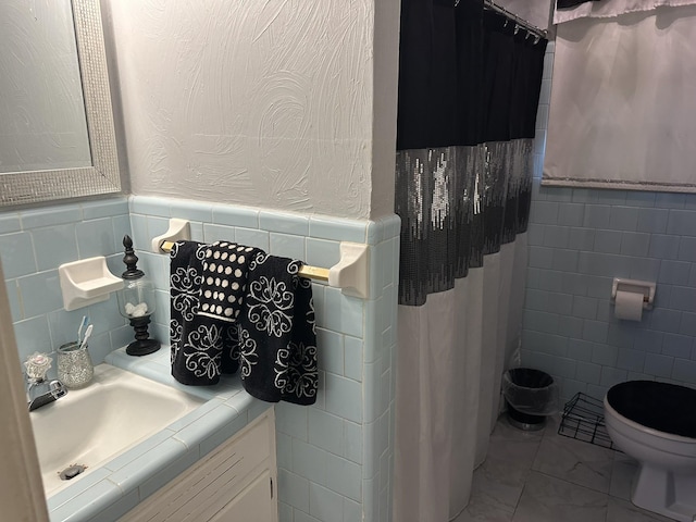 bathroom with toilet, vanity, and tile walls