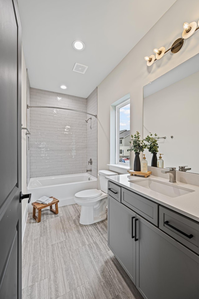 full bathroom featuring vanity, tiled shower / bath, hardwood / wood-style floors, and toilet