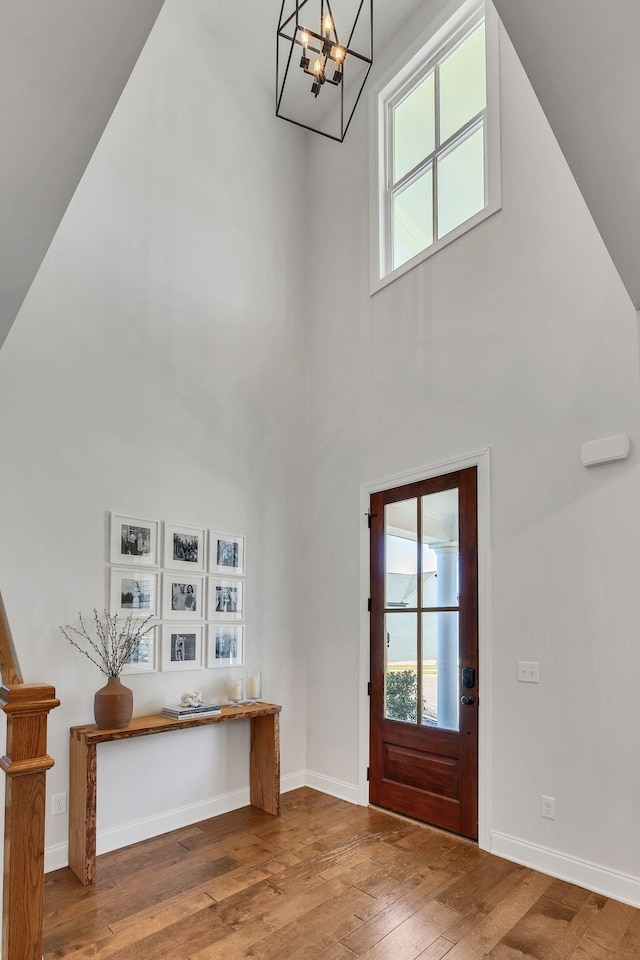 foyer entrance with a notable chandelier, wood-type flooring, and a high ceiling