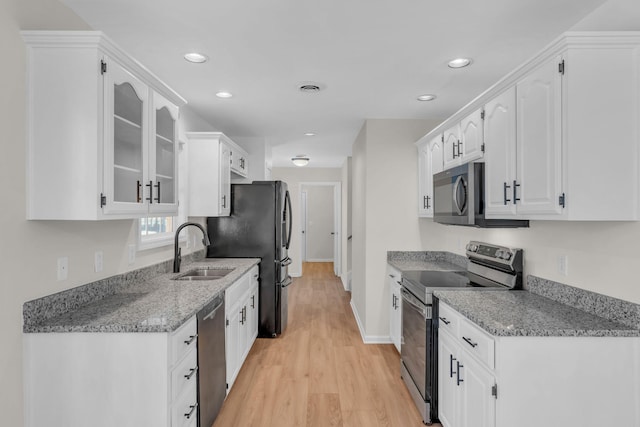 kitchen with sink, light stone counters, light wood-type flooring, stainless steel appliances, and white cabinets