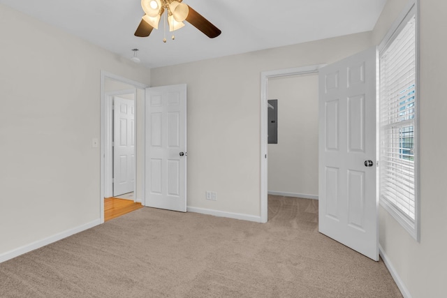 unfurnished bedroom with multiple windows, a walk in closet, light carpet, and electric panel