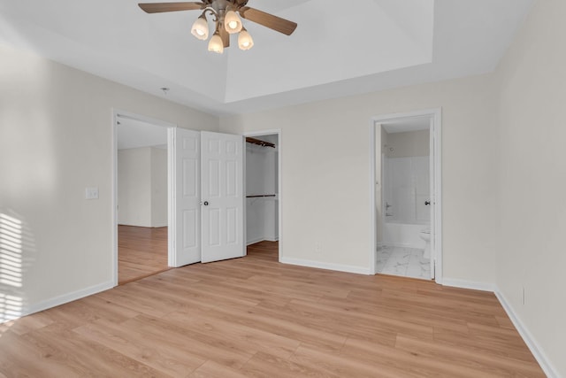 unfurnished bedroom featuring ensuite bathroom, a tray ceiling, a spacious closet, and light wood-type flooring