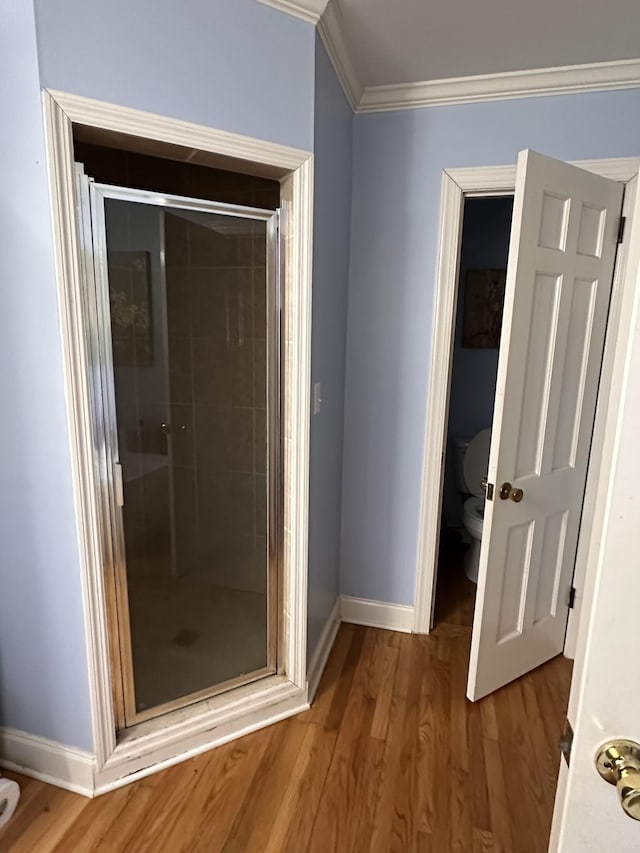 bathroom with toilet, wood-type flooring, a shower with door, and ornamental molding