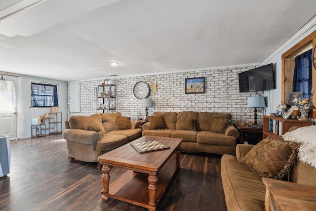 living room featuring dark wood-type flooring, ornamental molding, and brick wall