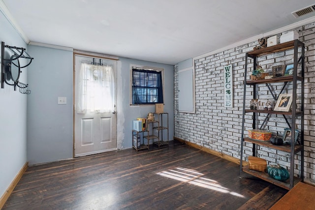 foyer with crown molding, dark hardwood / wood-style floors, and brick wall