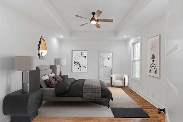 bedroom with ceiling fan, a tray ceiling, ornamental molding, and light wood-type flooring