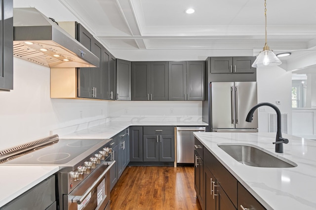 kitchen with premium appliances, wall chimney exhaust hood, sink, hanging light fixtures, and light stone counters