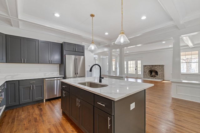 kitchen featuring a center island with sink, a brick fireplace, stainless steel appliances, light stone countertops, and sink