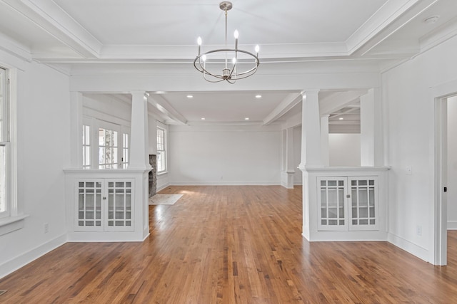 unfurnished dining area featuring beam ceiling, wood-type flooring, a notable chandelier, and ornamental molding