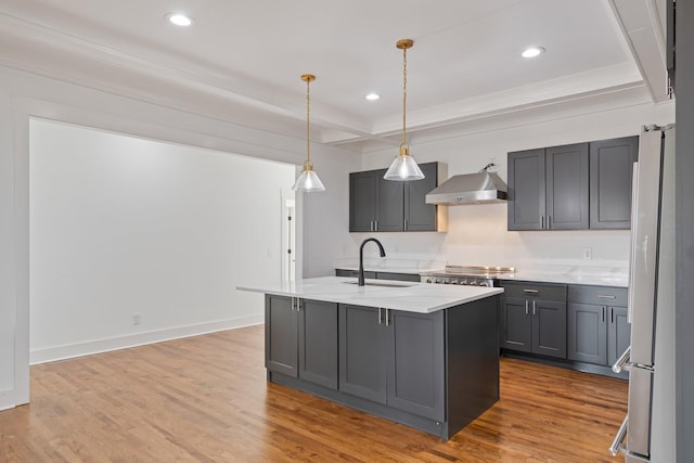 kitchen featuring refrigerator, gray cabinets, sink, an island with sink, and wall chimney exhaust hood