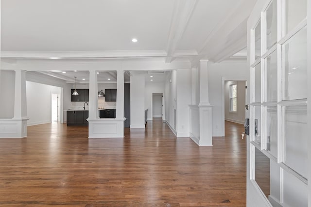 unfurnished living room featuring beamed ceiling, dark wood-type flooring, ornamental molding, and sink