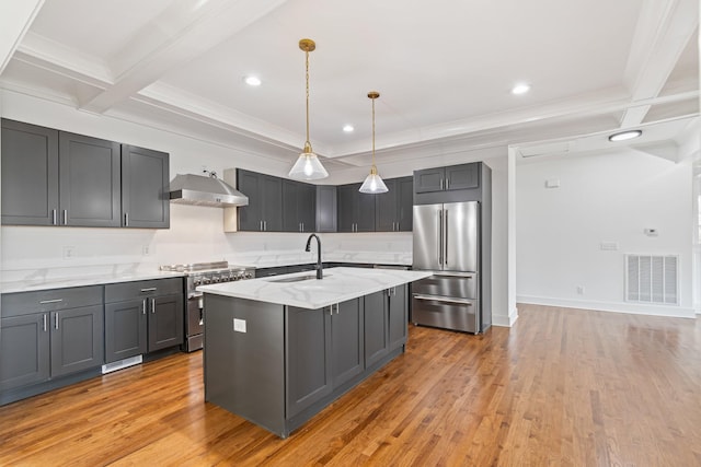 kitchen with wall chimney exhaust hood, an island with sink, sink, light stone counters, and high quality appliances