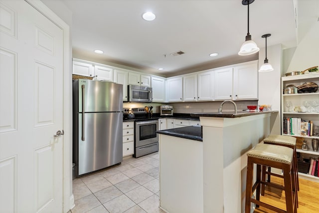 kitchen with white cabinets, a kitchen bar, stainless steel appliances, kitchen peninsula, and light tile patterned floors