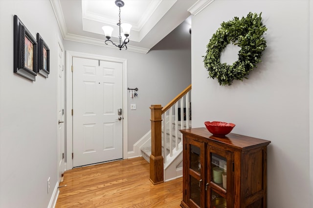 foyer entrance featuring a tray ceiling, light hardwood / wood-style flooring, crown molding, and a notable chandelier