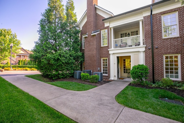 view of front of home with cooling unit, a balcony, and a front yard