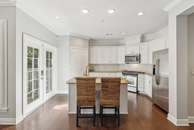 kitchen with tasteful backsplash, a kitchen breakfast bar, stainless steel appliances, a kitchen island with sink, and white cabinets