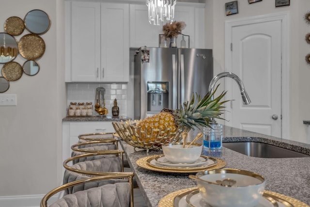 kitchen with stainless steel fridge with ice dispenser, decorative backsplash, dark stone counters, white cabinets, and sink