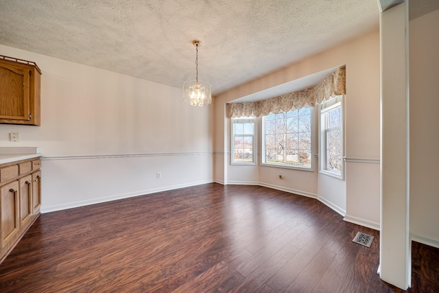 unfurnished dining area with a textured ceiling, dark hardwood / wood-style flooring, and a notable chandelier