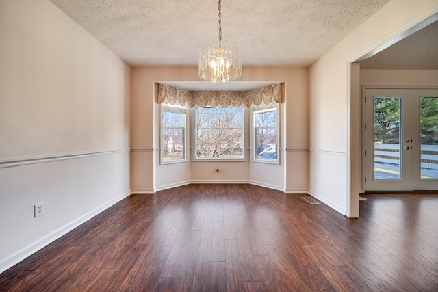 unfurnished dining area featuring a textured ceiling, a wealth of natural light, french doors, and an inviting chandelier