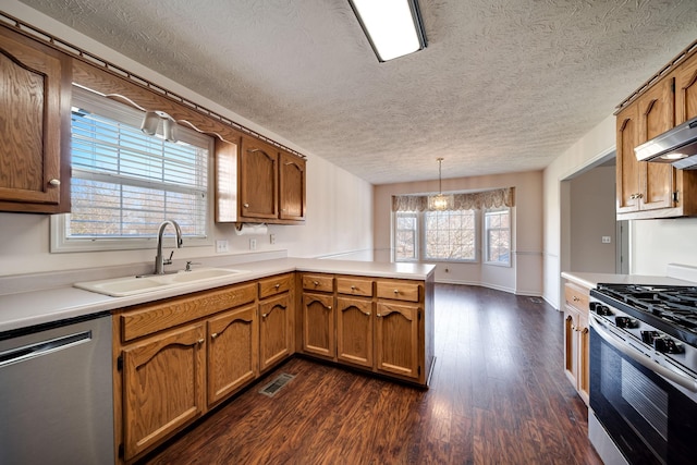 kitchen with a textured ceiling, appliances with stainless steel finishes, sink, hanging light fixtures, and kitchen peninsula