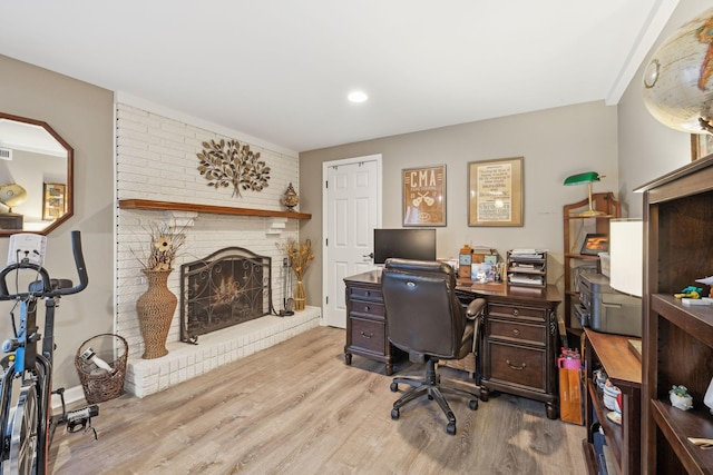 home office with light wood-type flooring and a fireplace