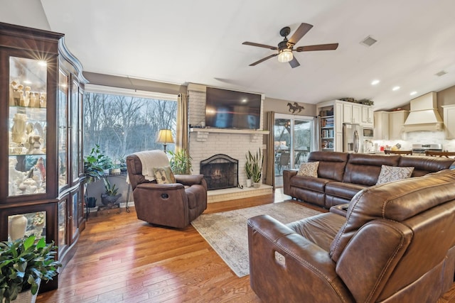 living room with ceiling fan, wood-type flooring, and a brick fireplace