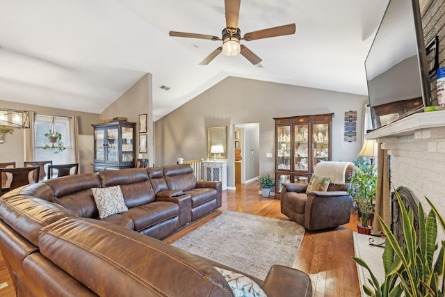 living room with vaulted ceiling, a brick fireplace, light hardwood / wood-style flooring, and ceiling fan