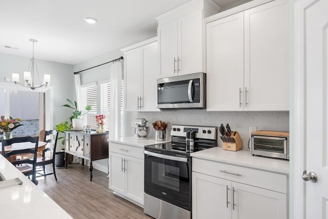 kitchen featuring white cabinetry, stainless steel appliances, backsplash, decorative light fixtures, and light wood-type flooring