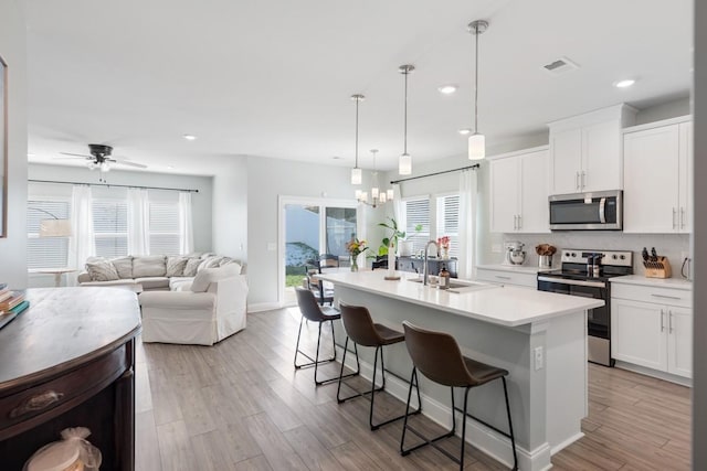 kitchen with pendant lighting, sink, white cabinetry, appliances with stainless steel finishes, and an island with sink