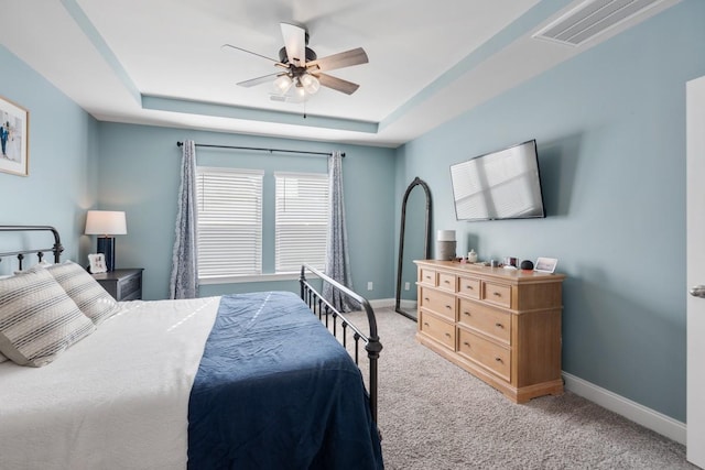 carpeted bedroom with ceiling fan and a raised ceiling