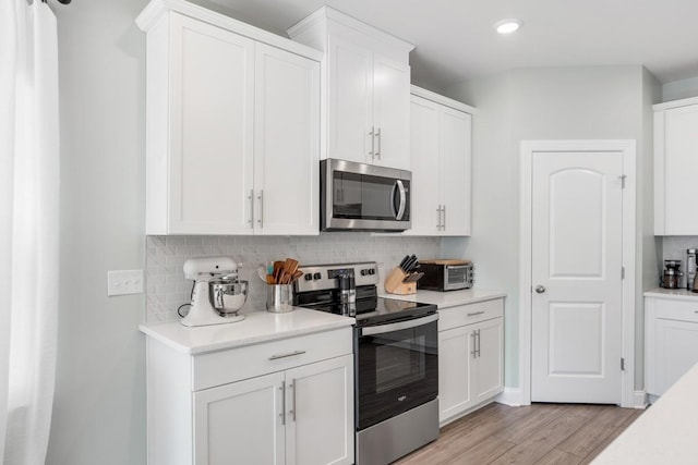 kitchen with light wood-type flooring, appliances with stainless steel finishes, decorative backsplash, and white cabinetry