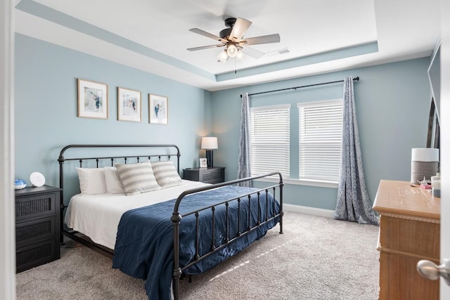 carpeted bedroom with ceiling fan and a tray ceiling