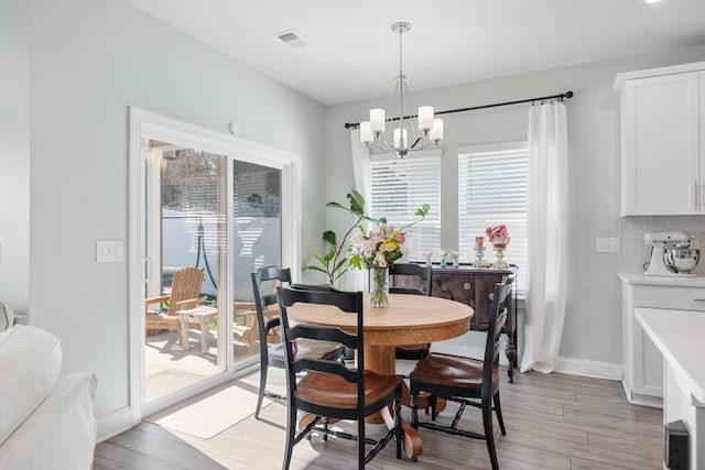 dining room featuring light wood-type flooring, plenty of natural light, and a notable chandelier