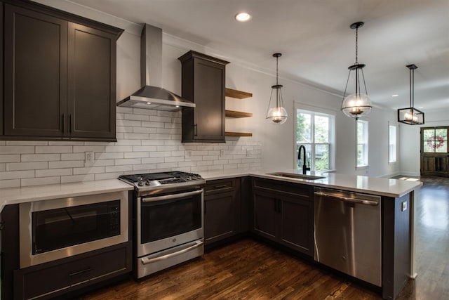 kitchen with wall chimney exhaust hood, sink, hanging light fixtures, appliances with stainless steel finishes, and kitchen peninsula