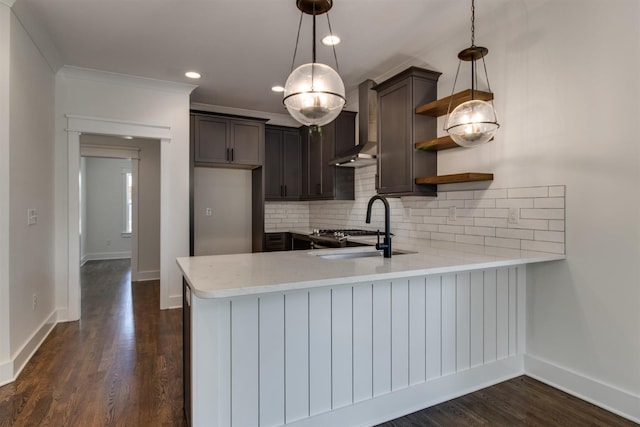 kitchen featuring pendant lighting, sink, kitchen peninsula, and wall chimney exhaust hood