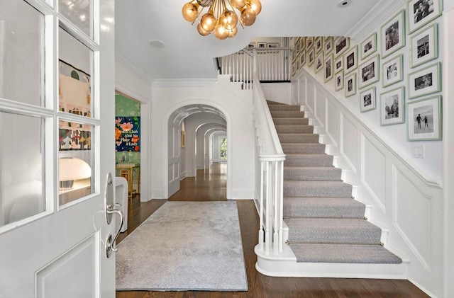 entrance foyer featuring dark wood-type flooring, a chandelier, and ornamental molding