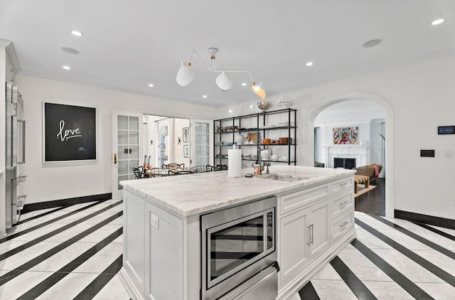 kitchen with light stone countertops, white cabinets, stainless steel appliances, sink, and a center island with sink