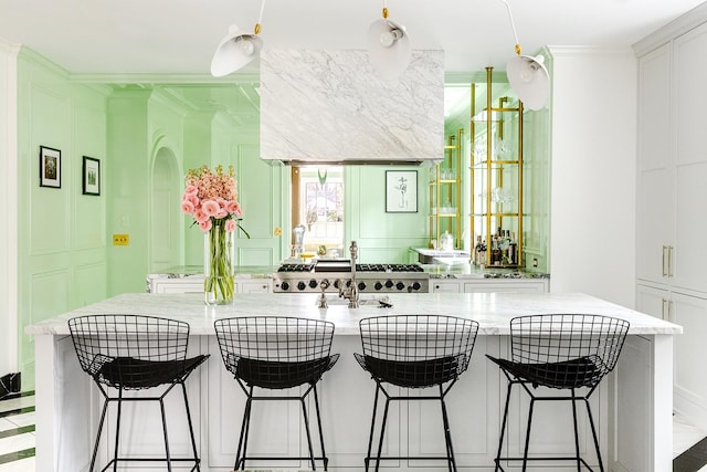 kitchen featuring a center island with sink, a breakfast bar area, white cabinets, and light stone countertops